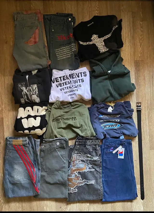 Jeans, zip-up hoodies, Carhartt and Far Archive tops, and a belt laid out on a wooden floor in the original 10kg Sugargoo haul